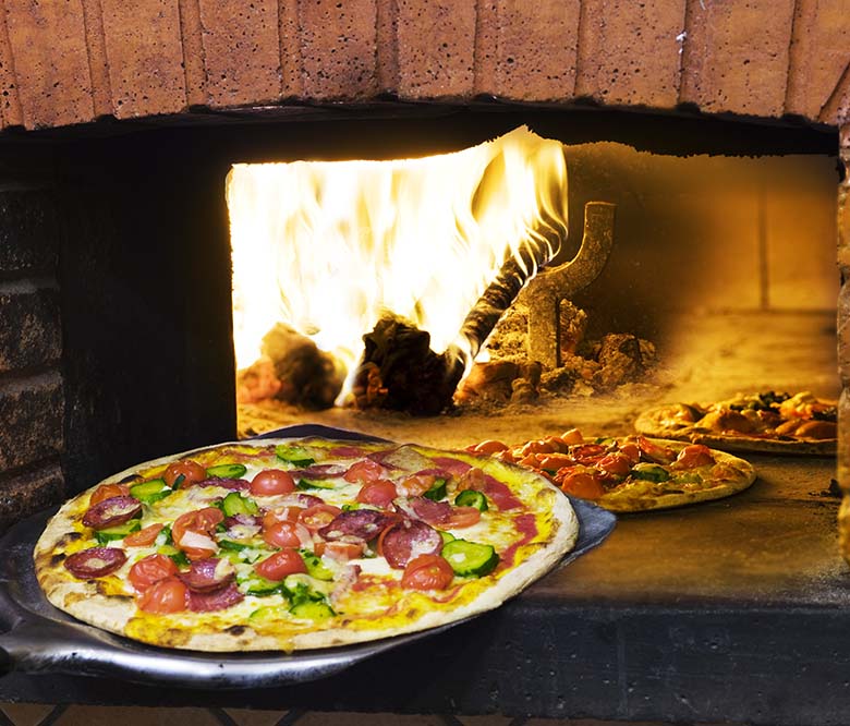 pizza coming out of a wood burning pizza oven.